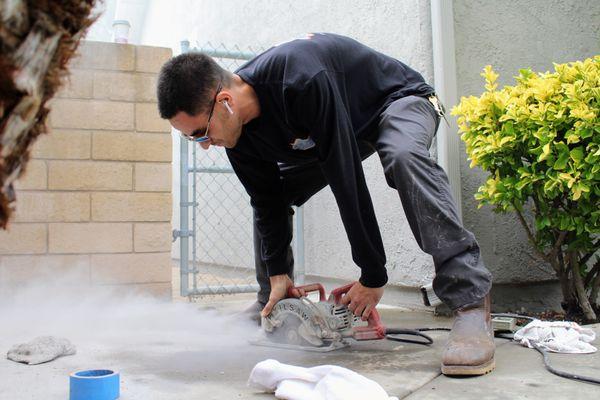 Gabe with the use of a skill saw cutting into the concrete exposing the line.