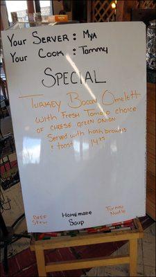 A white board is located next the counter, where the daily specials are listed.  It also gives the name of the restaurant staff on duty.