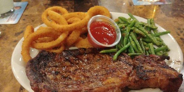 Well-done ribeye steak with green beans and onion rings.