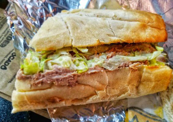 Tuna Crunch out of its paper wrapping. You can see the lettuce and the tuna salad within it. There are also a few chips and tomatoes.