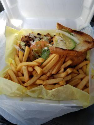 A well dressed torta al pastor with fries.