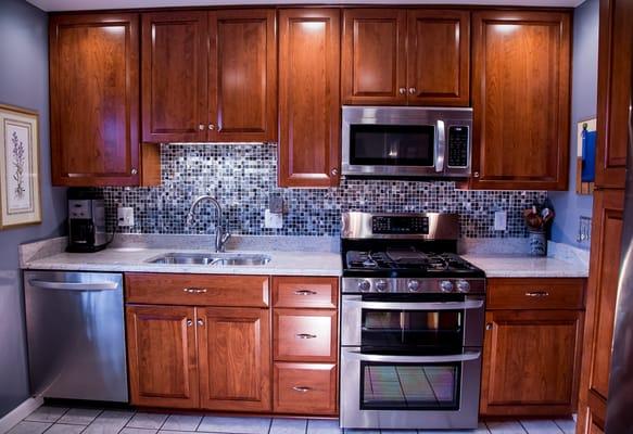 Cherry raised panel doors and cabinets add a warm counterpoint to the cool blues and greys in the backsplash and walls of this kitchen.