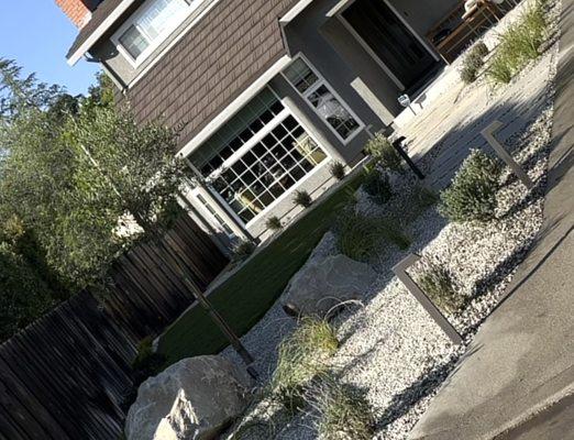 Planter area set all around with pebbled rock, tree set in between large boulders, walkway light set up