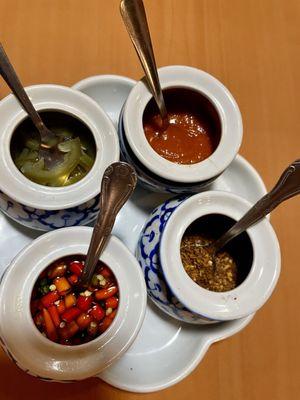 Table condiments: jalapenos in vinegar, sriracha, thai chiles in fish sauce, and crushed peppers