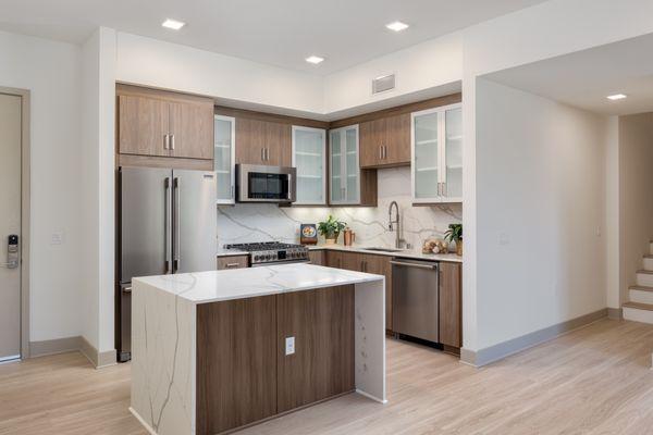 Modern kitchen with upscale dark wood finished cabinetry and  marble style waterfall counter tops.