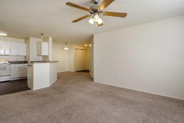 Living room with carpet flooring, multi speed ceiling fan, and kitchen in the background