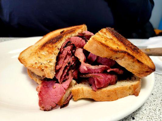 Pastrami sandwich on grilled rye bread with a side of Mac salad