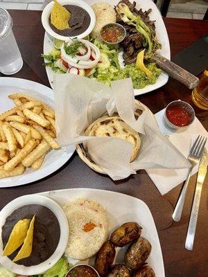 Steak and sausages rice beans salads bread and French fries