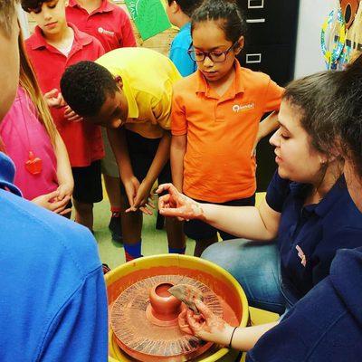 Elementary students learning how to throw a pot on the wheel.