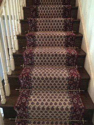 Runner showing 3" of wood on both sides with brass stair rods with pineapple end caps.