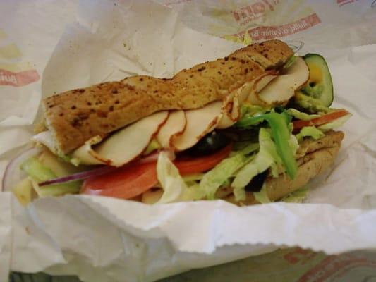 Turkey sandwich with honey oat bread, lettuce, tomatoes, onions, bell peppers, olives, cucumbers, mustard, and 'avocados.'