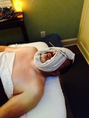 Actual client relaxing at the end of session with an essential oil soaked hot towel on his face