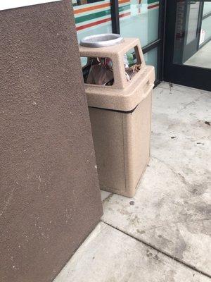 Overflowing trashcan and stained concrete from liquid spills of a store that has not been opened one month yet