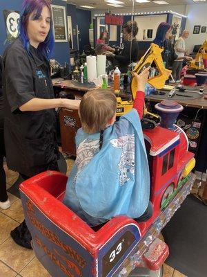 Sarah with her young client sitting in the choo choo train chair that raises and lowers like a real barbers chair.