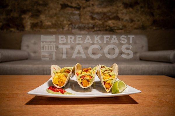 Breakfast Tacos, scrambled eggs, red peppers, potatoes, bacon on a flour taco shell with avocado sauce.