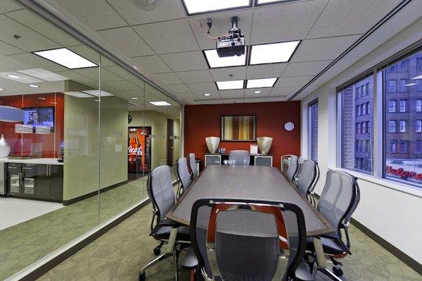 A modern conference room featuring a long rectangular table surrounded by ergonomic office chairs with mesh backs...