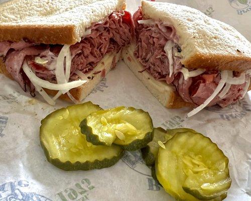 Whole Pastrami Sandwich with white onion, Russian dressing, Swiss cheese on white bread and a side of dill pickles.