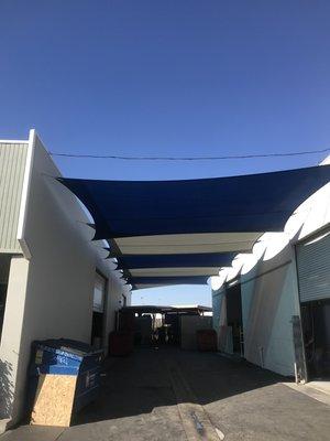 Overlapping (true blue and pearl onyx) sail shades between two commercial buildings.