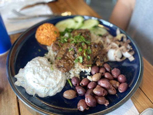 Sirloin kebab over rice pilaf platter with olives, cucumbers, and onion with sumac. Tzatziki sauce and roasted red pepper sauce.