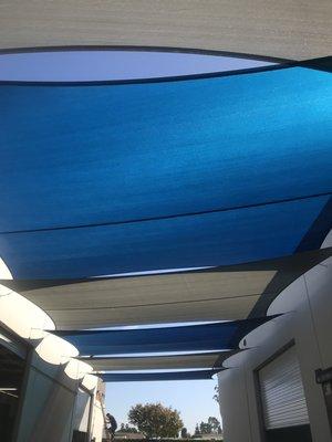 Overlapping (true blue and pearl onyx) sail shades between two commercial buildings.