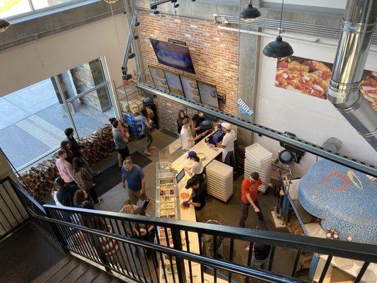 Entrance, order counter, pizza oven, and open preparation area, taken from the upstairs dining area.