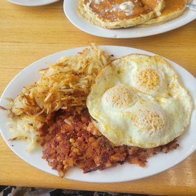 Corned beef and hash with 3 over easy eggs, hash browns and 2 pancakes.