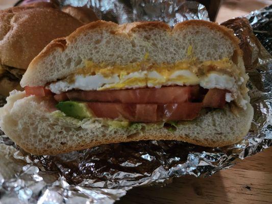 Eggs, cheese, avocado and tomatoes on a roll.