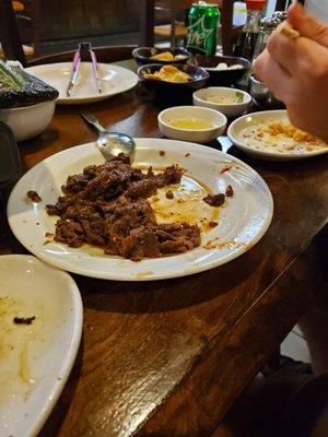 Spicy beef after being cooked on the hot plate. Side dishes in the back.