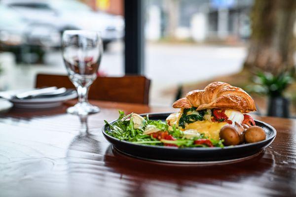 Breakfast croissant with poached egg, side of potatoes and salad.