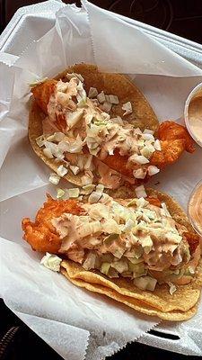 Two fish tacos with veggies on top and chipotle sauce.