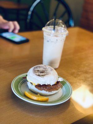 Bacon, Sausage Egg And Cheese Breakfast Sandwich on an English muffin.  Iced Caramel Macchiato in the back.