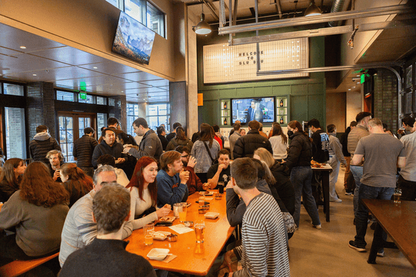 The busy interior of SLU BRU is filled with people socializing and enjoying food and drinks, with TVs displaying sports in the background.