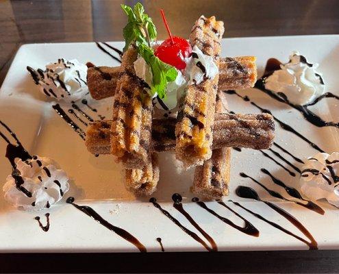 Churros with chocolate sauce drizzle, whip cream accents, and a cherry on top