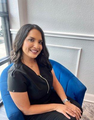 Priti Patel, sitting in a blue chair. She is the clinical director and owner.