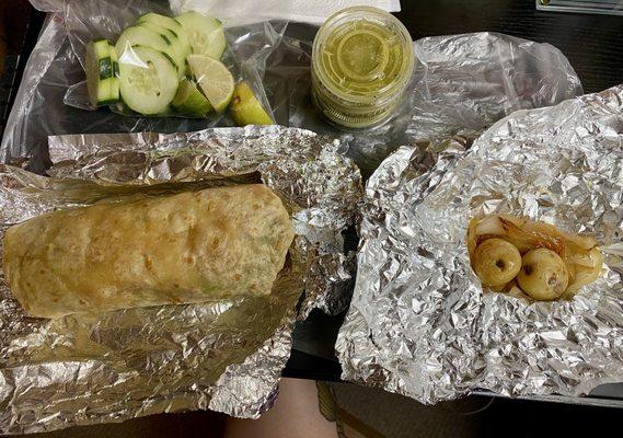 Veggie burrito with green salsa, potatos and onions and fresh slices of cucumbers and limes.