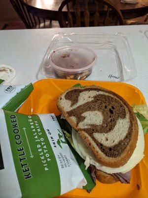 Marble rye sandwich with chips and side dish.