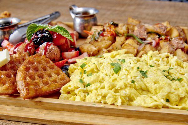 Brunch Charcuterie Board with waffle battered chicken, candied bacon, sausage, house potatoes & scrambled eggs. Served with churro waffles