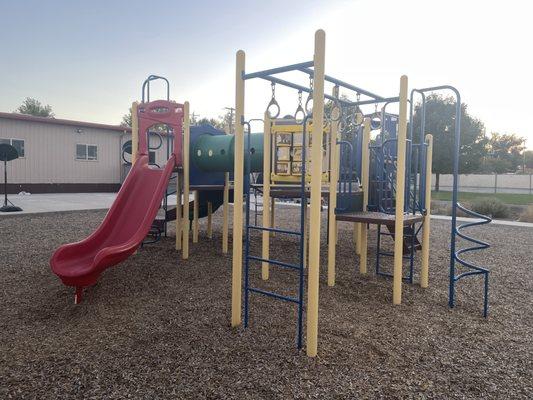 Back playground. Monkey bars and tunnel with a red slide.