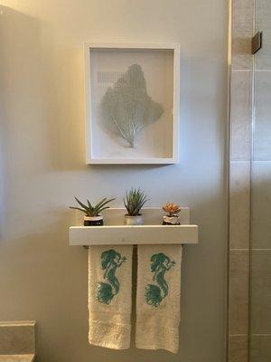 Shelving above the toilet with succulents, ethically sourced coral artwork, mermaid towels (all from Etsy)