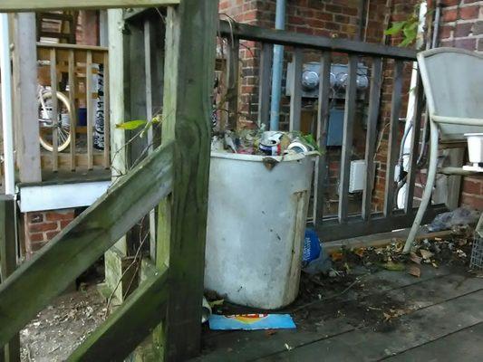 Overflowing trash receptacle stored on porch for a minimum of several years.