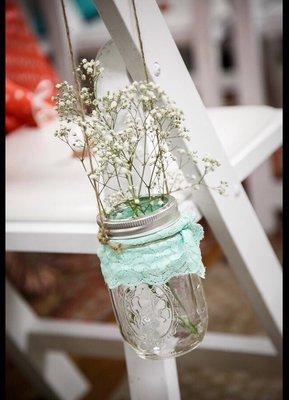 Rented white wooden chairs decorated with handing mason jars and babies breath