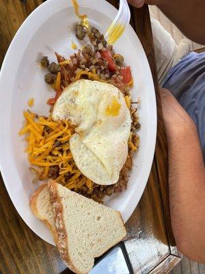 Eggs atop of mixed meat and potatoes with toast