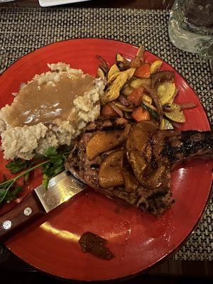 Pork chop with apple topping, mashed potatoes with gravy, and veggies