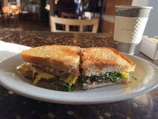 Bacon, arugula and egg sandwich with a cup of coffee.