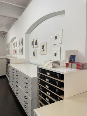 View of righthand side of gallery interior, showing storage boxes, books, and framed artworks on display