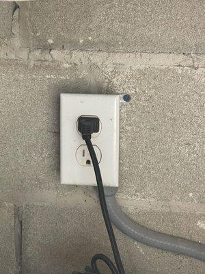 Non-gfci outlet under grill where residents hook up electric cords for devices around pool.