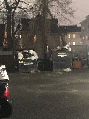 Overflowing trash with broken glass around dumpsters