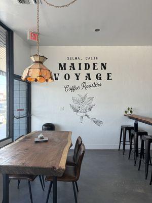 To the left: Table and chairs by window To the right: an L shaped bar with stools