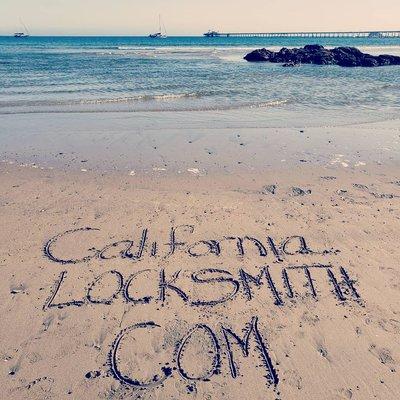 "Californialocksmith.com" written in the wet beach sand with the ocean beautiful behind it.