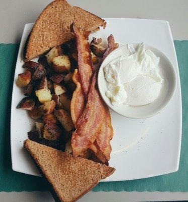 Poached eggs with home fries, toast, and a side of bacon.